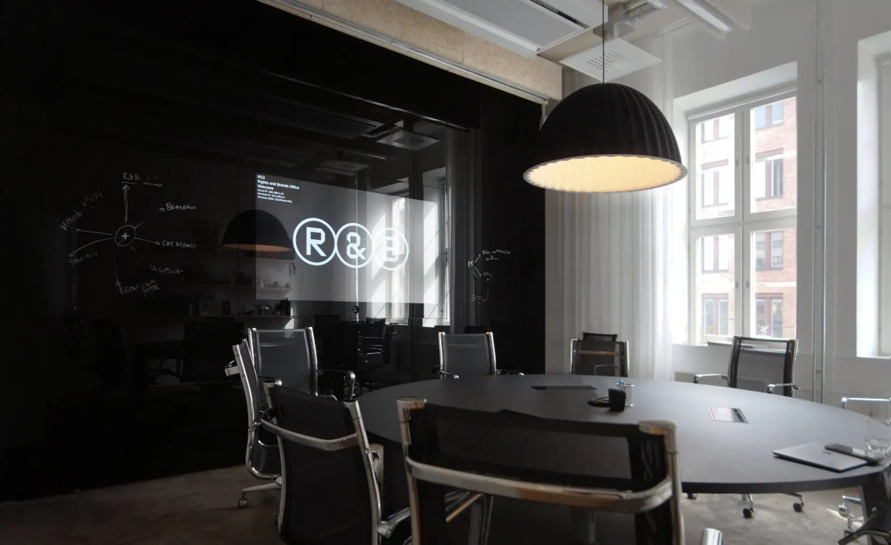 Mörkt styrelserum med ovalt bord, svarta läderstolar och en skrivbar glasvägg